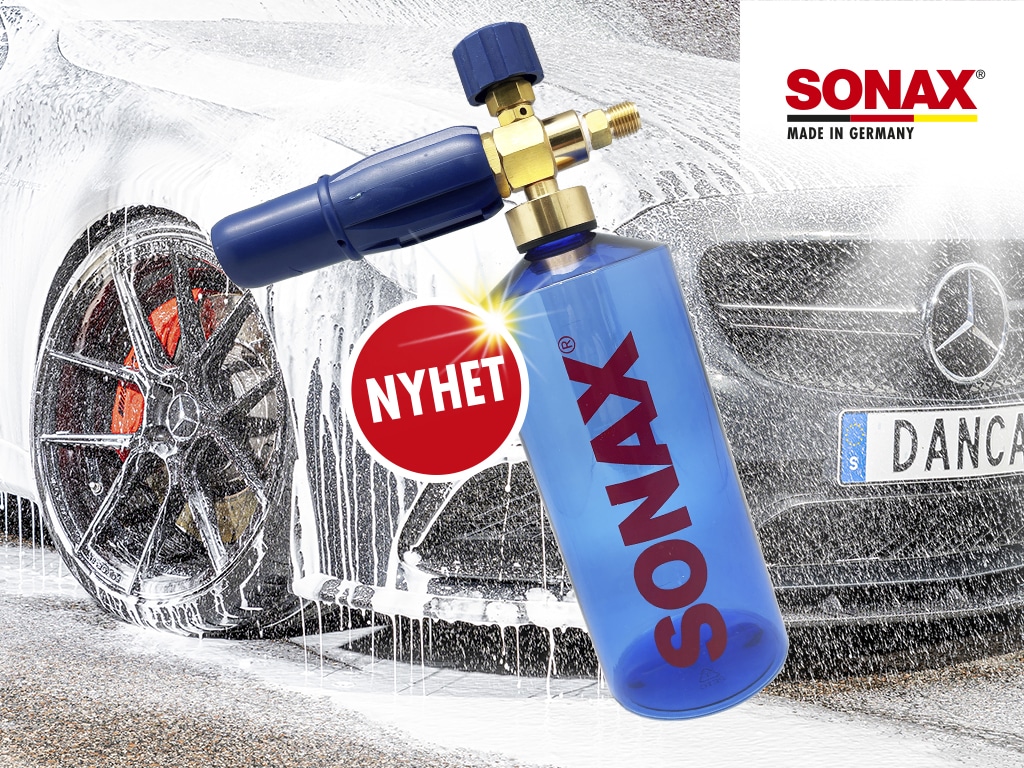 Foam lance flaska i blå plast och munstycke från SONAX med NYHET-badge i rött. Produkten syns i förgrunden av foamskummad mörkgrå Mercedes.