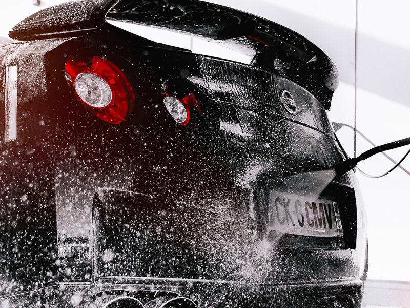 Bilvård på schamponerad svart sportbil som spolas ren med högtrycksspruta.
